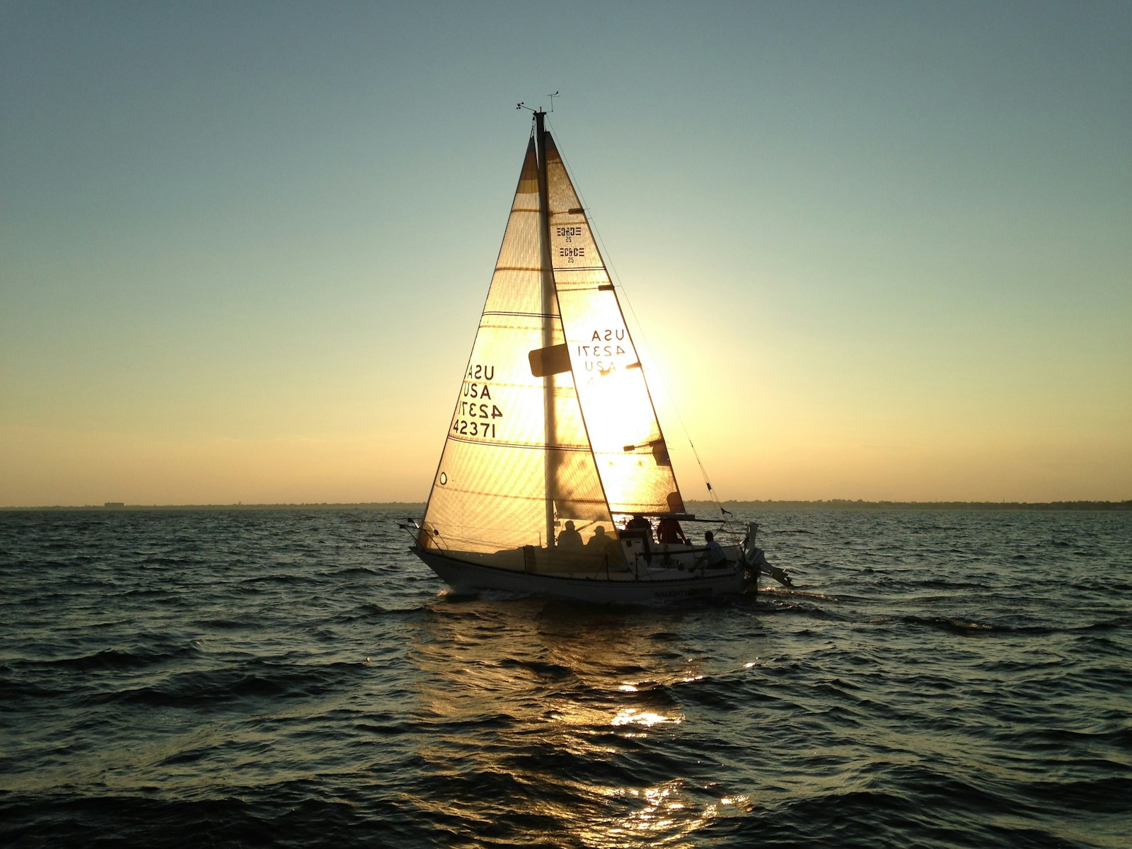 A sailboat and its crew on calm water in evening light